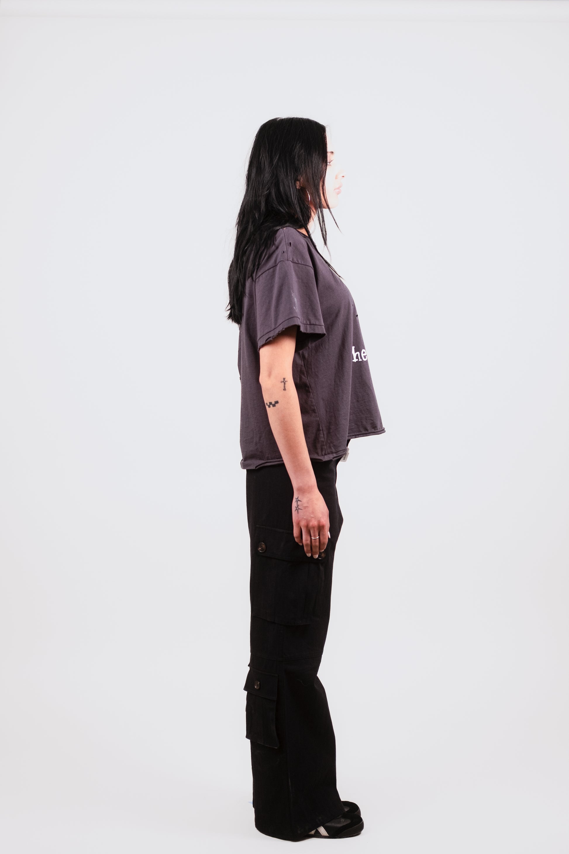 Female model alternate profile in the Puppets Punk Tee — fashion-forward boxy crop tee in vintage black with edgy punk graphic and raw cap sleeves.