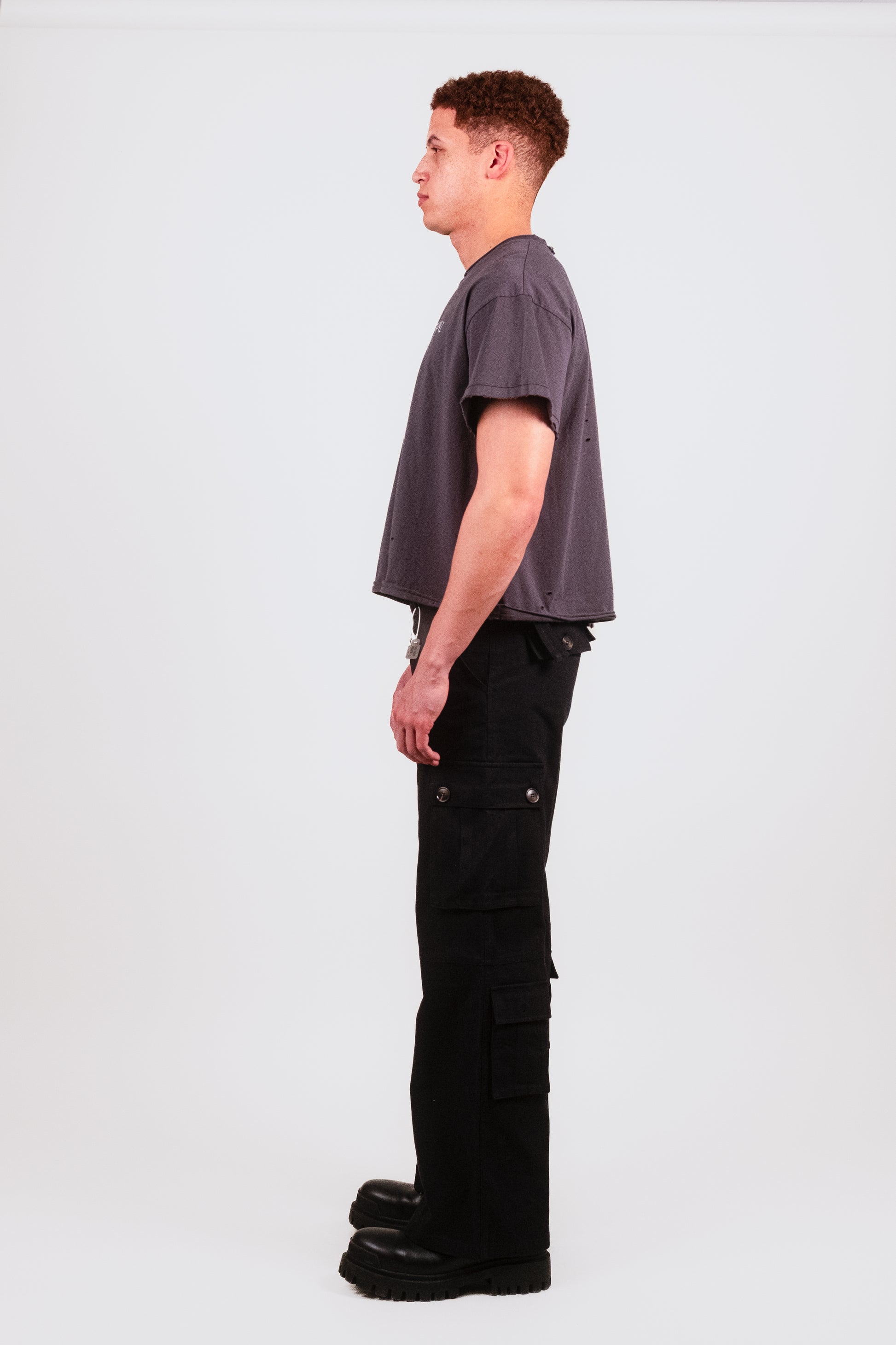 Profile shot of male model wearing Puppets Punk Tee — distressed black boxy t-shirt in fine cotton with cropped cap sleeve cut and punk graphic detailing.