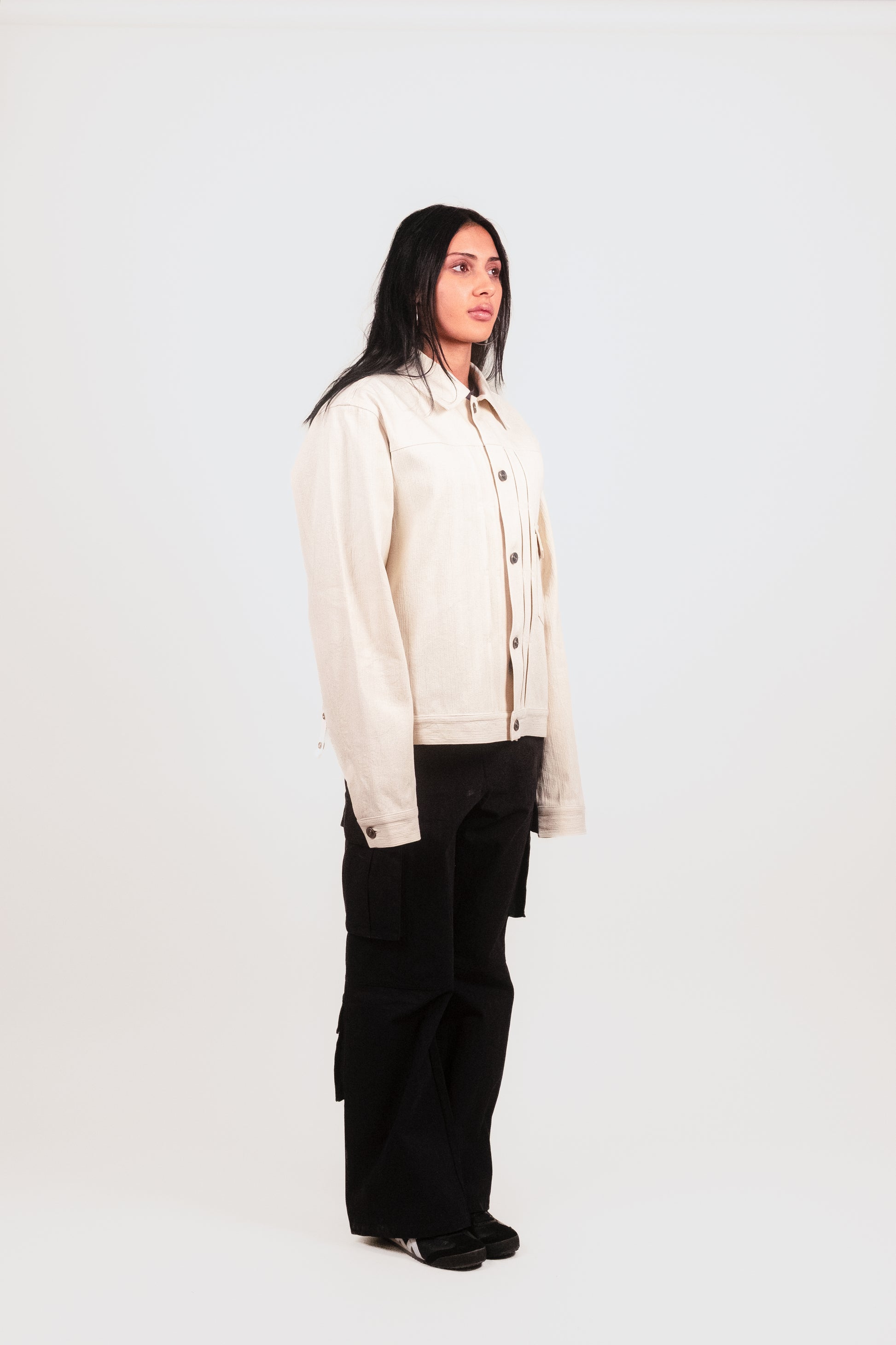Female model alt 1/4 angle in Pleated Military Blouson — sculptural off-white jacket with pleats, drape, and modular closure design