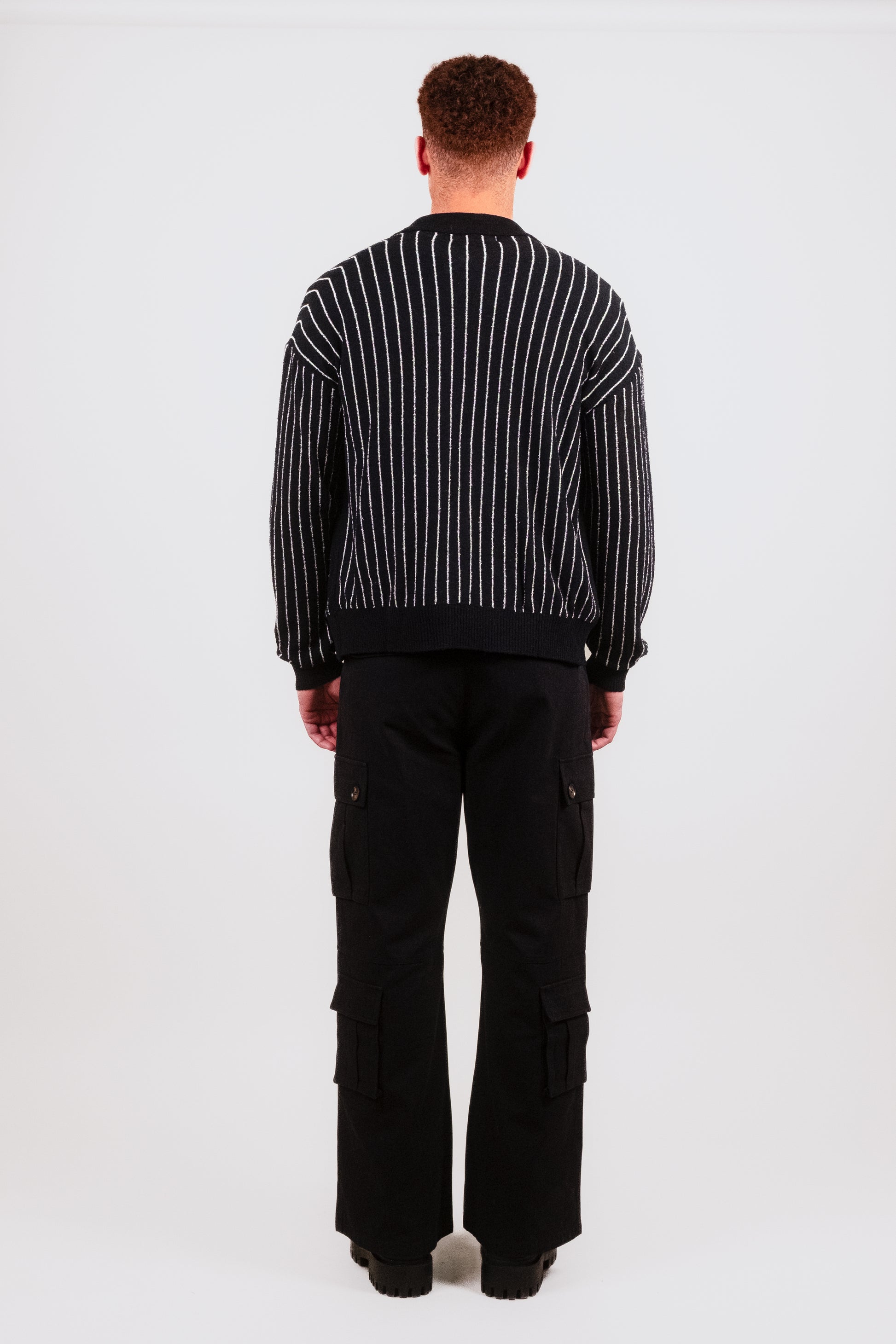 Rear view of Nate in the Posh Full Zip black, highlighting the clean knit back detail, white pinstripe pattern, and expertly tailored fit from Puppet Theater’s luxury collection.