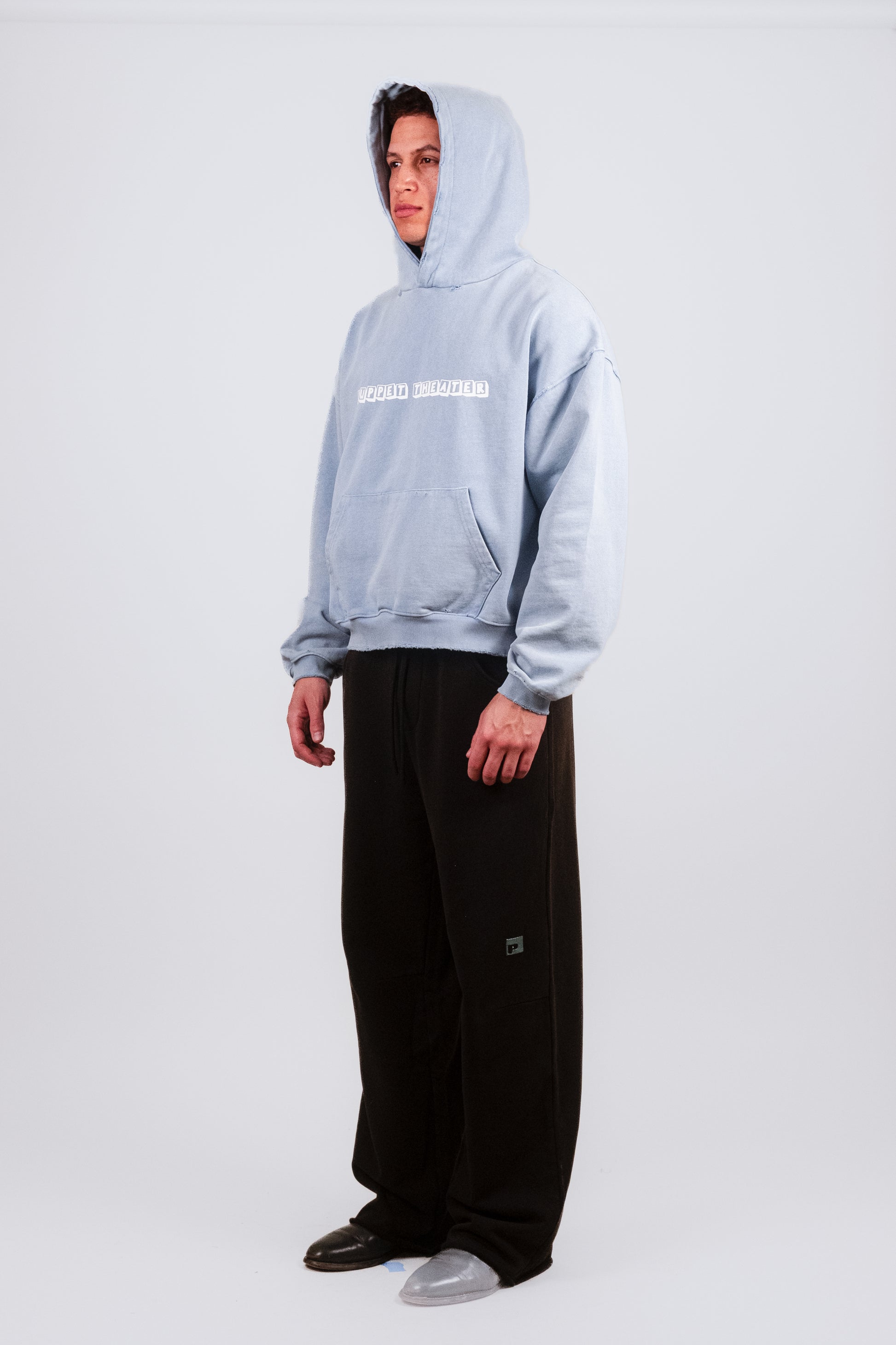 Quarter angle on Nate wearing the Reminiscence Block Logo Hoodie — showing the softly aged fleece texture, cropped relaxed silhouette, and faded toy block graphic on the front. This designer hoodie blends luxury streetwear energy with a personal archival reference to Denver’s Puppet Theater.