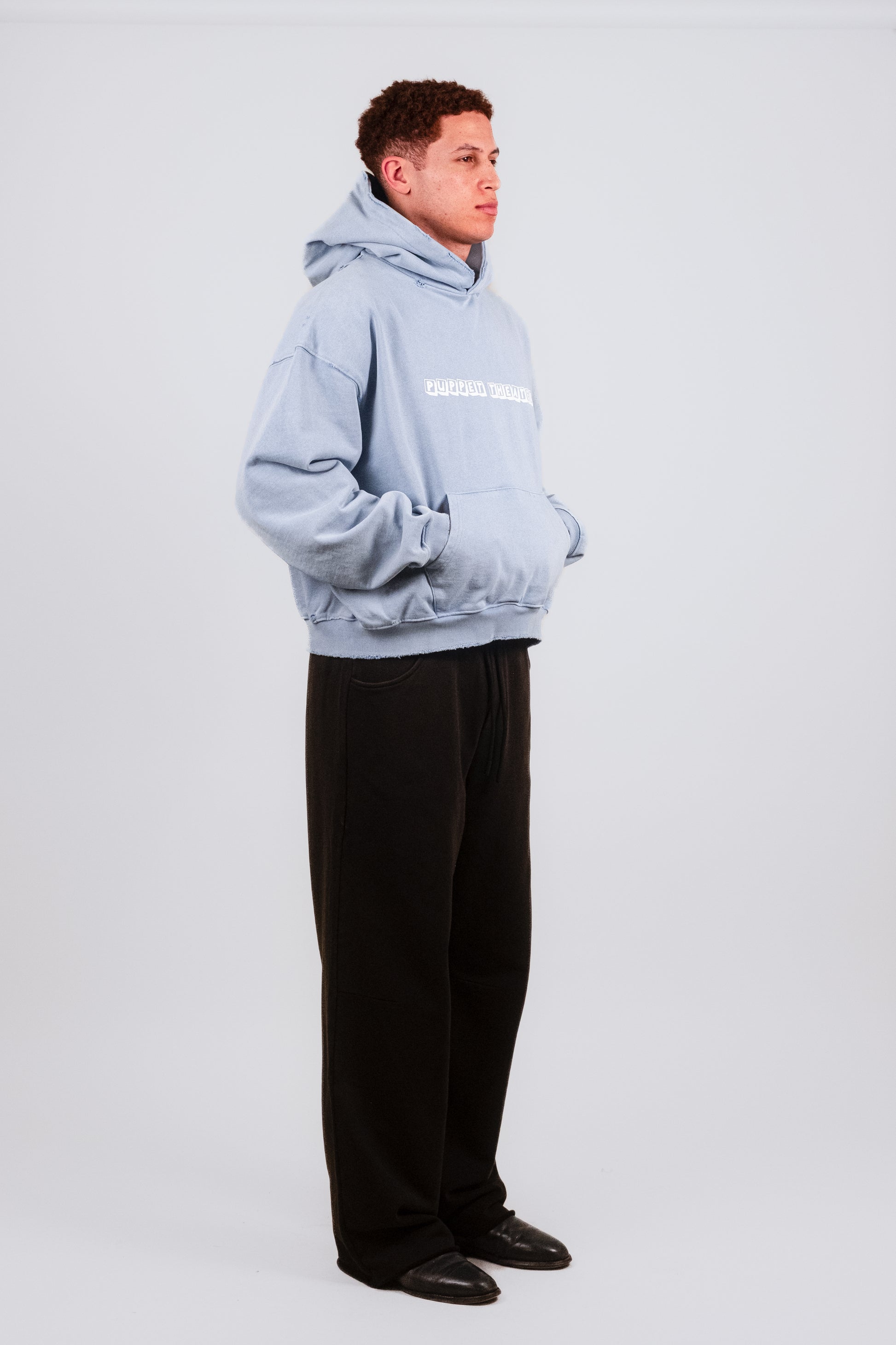 Alternate quarter angle of Nate wearing the Reminiscence Block Logo Hoodie — premium washed cotton and faded baby blue fleece combine with vintage cuff distressing, nostalgic graphics, and boxy designer proportions for a timeless streetwear silhouette.