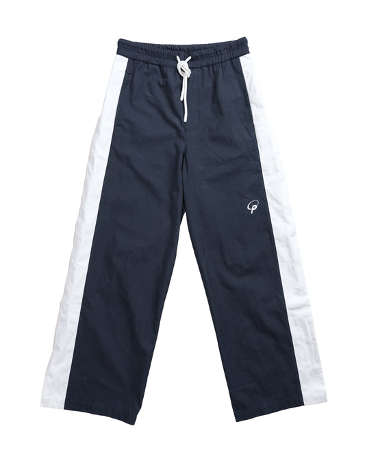Flat lay front of the Sports Bottom — designer track pant silhouette in technical nylon with a crisp straight leg and hidden side snap closures under a clean white stripe.